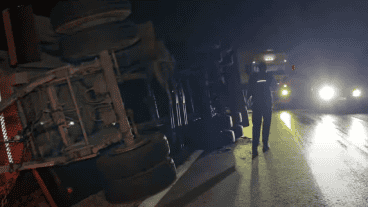 El camionero junto al acoplado de su camión, visiblemente volcado hacia la banquina, mientras pasaban otros vehículos a su lado.