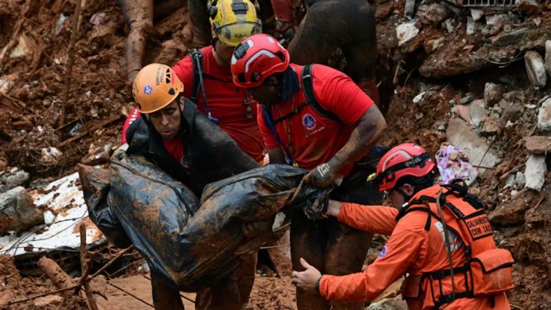 Los bomberos cargan un cadáver encontrado entre los escombros tras un deslizamiento de tierra causado por las fuertes lluvias en el Barrio Parque Jardim Burnier, en Juiz de Fora, Estado de Minas Gerais, Brasil.