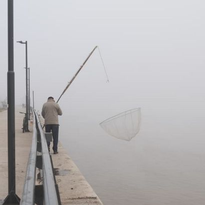 Un pescador se "pierde" en medio del gris que la niebla esparce en la ribera.
