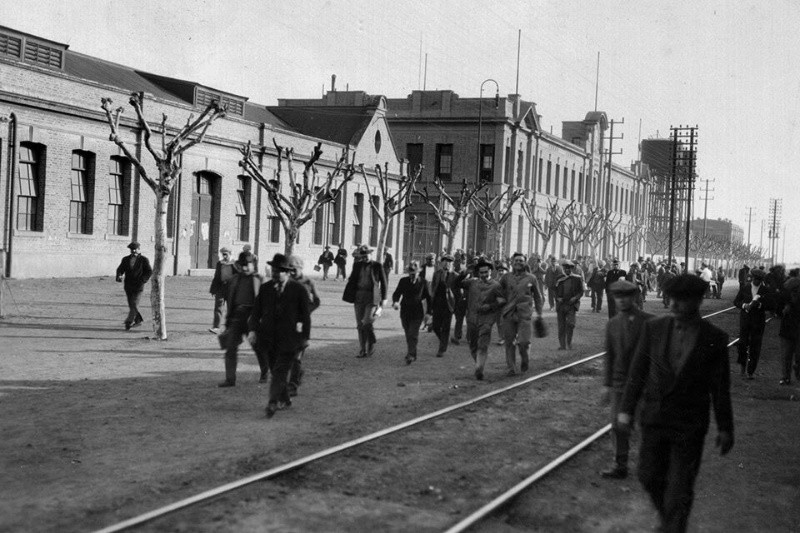 Ferroviarios salen tras cumplir su jornada. De fondo, la fachada de los talleres en la década de 1930.
