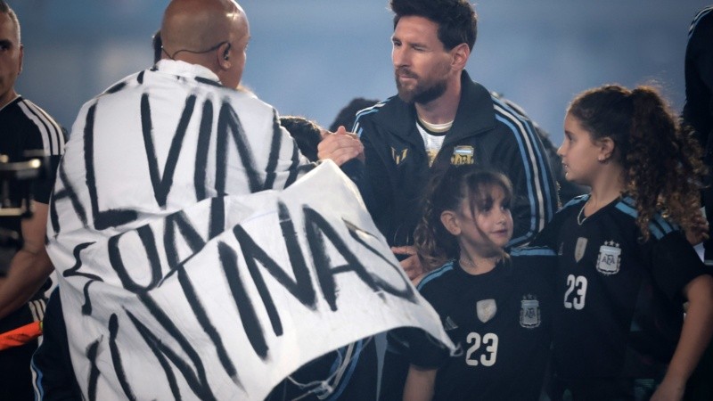 El saludo de Fabio Santana, envuelto con la bandera de Malvinas, y Leo Messi después del himno.